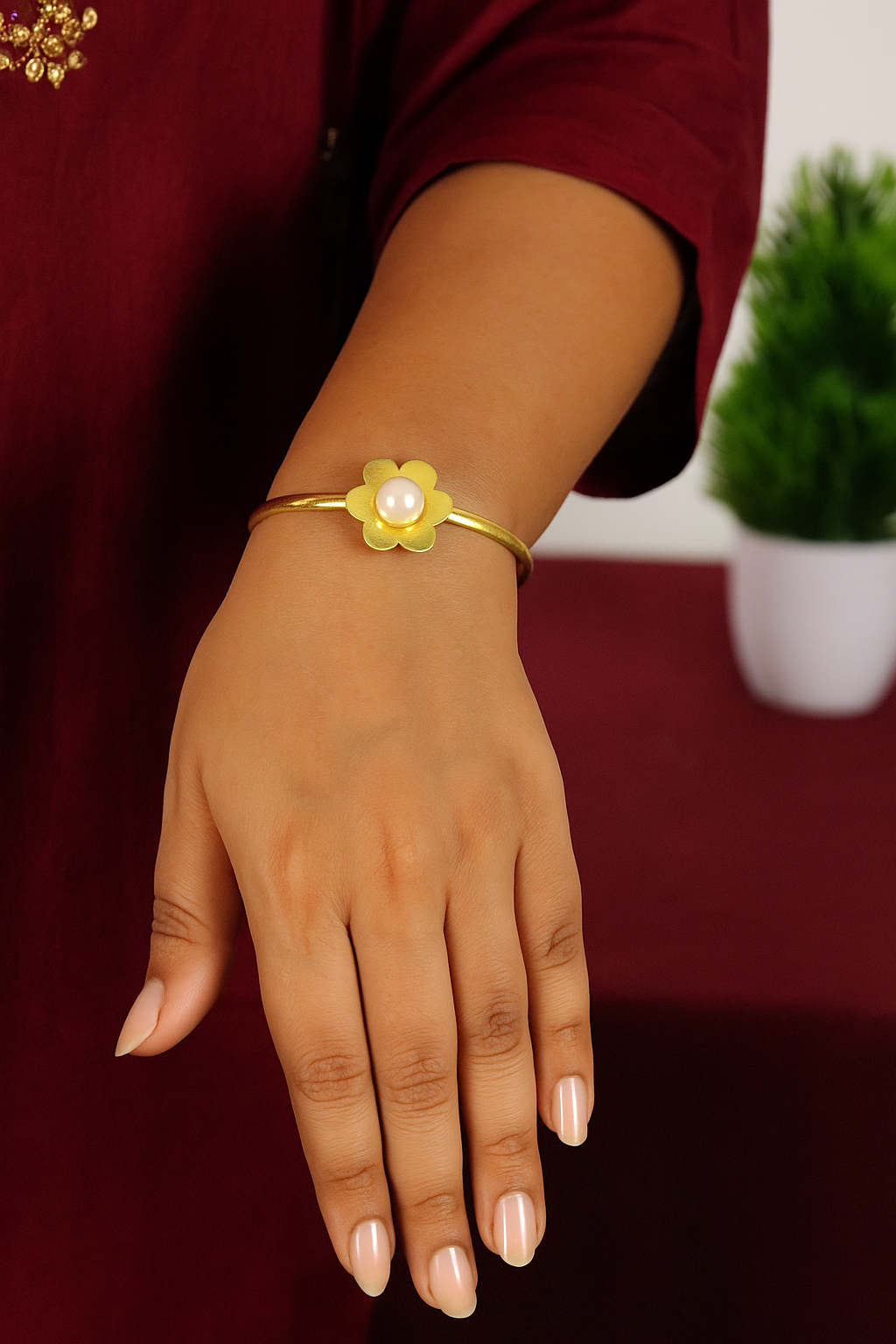 Hand wearing a gold bracelet with a floral design